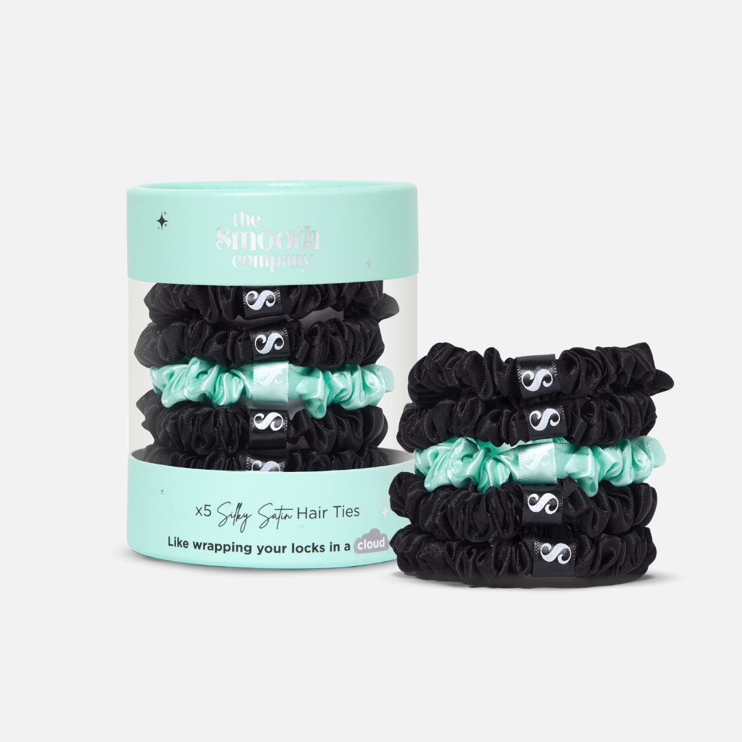Packaging of five silky satin hair ties in black, green, and blue colors, displayed in a clear plastic container with a blue lid, next to a pile of hair ties. 